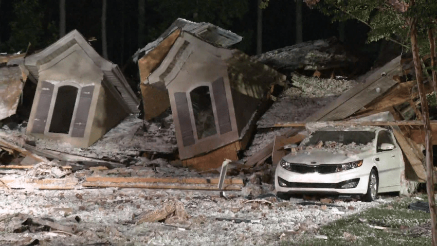 Destroyed house following an explosion with a white car next to it.