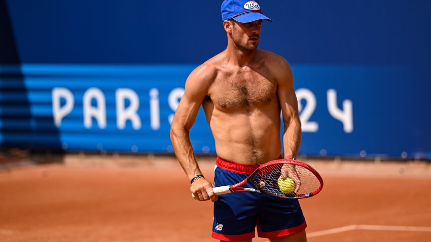 Shirtless Tommy Paul on red clay tennis court.